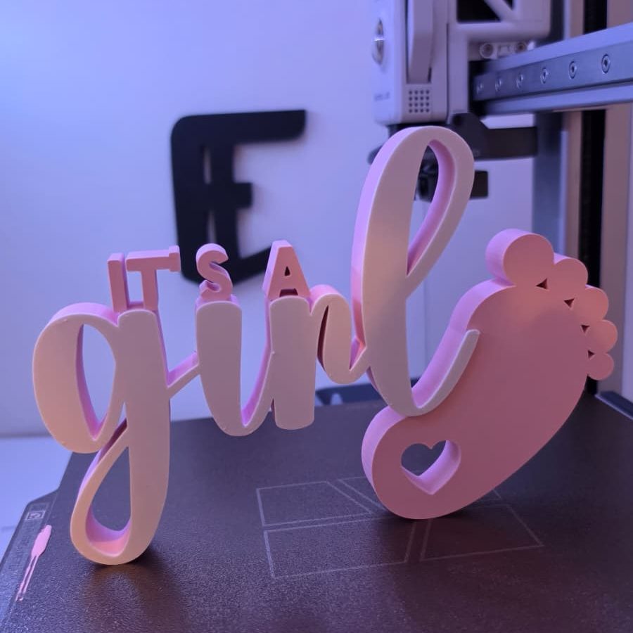 Wortkunst „It's a girl“ mit pinkem Fußabdruck und weißem Schriftzug.