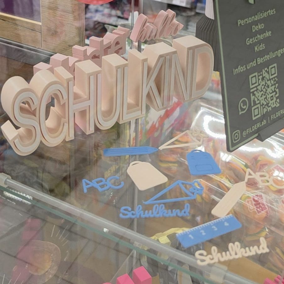 Holzschriftzug "SCHULKIND" mit bunten Anhängern in einem Schaufenster.